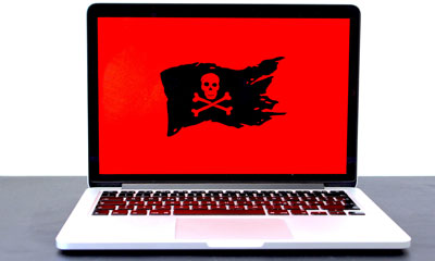 A laptop computer displaying a red background with a pirate flag logo on top signifying that the computer has been targeted by ransomware.